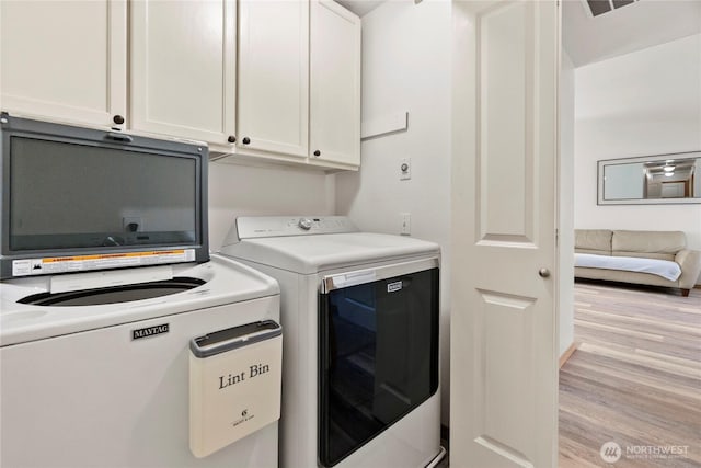 laundry area featuring washer and dryer, cabinet space, and light wood-style floors