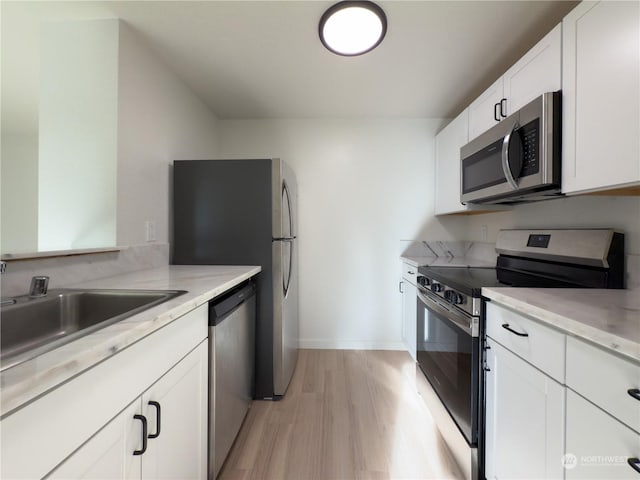 kitchen with sink, white cabinetry, stainless steel appliances, light stone counters, and light hardwood / wood-style floors