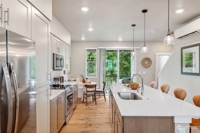 kitchen featuring sink, white cabinetry, hanging light fixtures, stainless steel appliances, and an island with sink