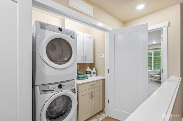 laundry area featuring stacked washer / drying machine and cabinets