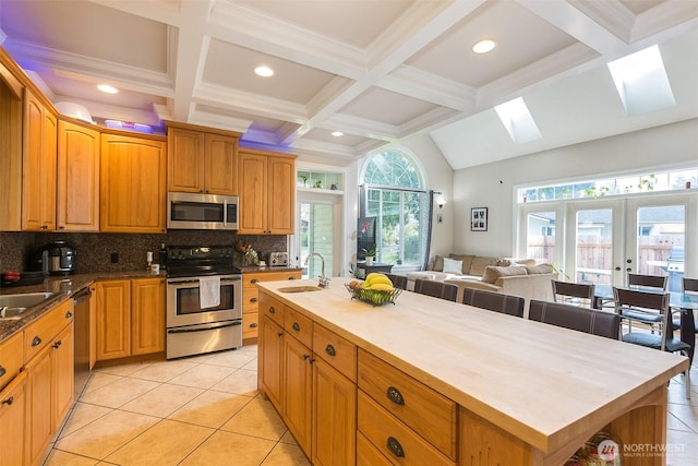 kitchen featuring a skylight, tasteful backsplash, appliances with stainless steel finishes, french doors, and a sink