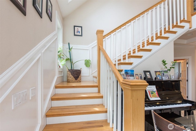 stairs with a wainscoted wall, vaulted ceiling, wood finished floors, and a decorative wall