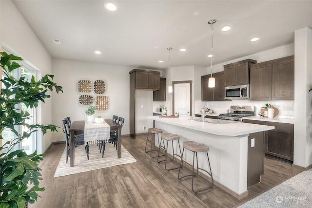 kitchen with dark wood-type flooring, range, decorative light fixtures, dark brown cabinets, and an island with sink