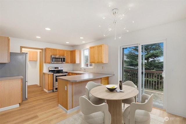 kitchen with sink, kitchen peninsula, stainless steel appliances, light brown cabinets, and light hardwood / wood-style flooring