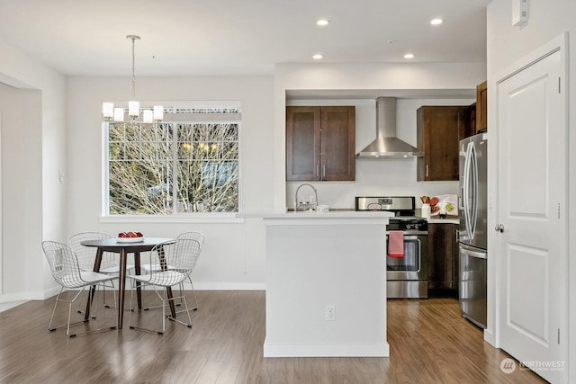 kitchen featuring hanging light fixtures, hardwood / wood-style floors, wall chimney exhaust hood, and appliances with stainless steel finishes