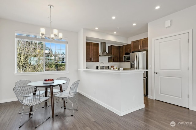 kitchen with dark wood-type flooring, appliances with stainless steel finishes, decorative light fixtures, and wall chimney range hood