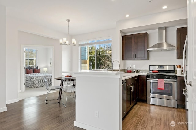 kitchen featuring hardwood / wood-style flooring, appliances with stainless steel finishes, wall chimney range hood, and kitchen peninsula