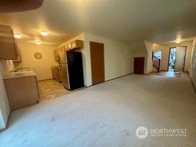 kitchen featuring light carpet, light brown cabinetry, sink, and stainless steel refrigerator