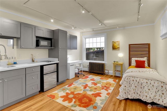 bedroom with sink, crown molding, stainless steel fridge, radiator heating unit, and light wood-type flooring