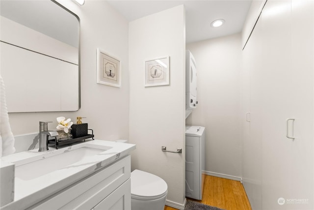 bathroom with toilet, vanity, stacked washing maching and dryer, and hardwood / wood-style flooring