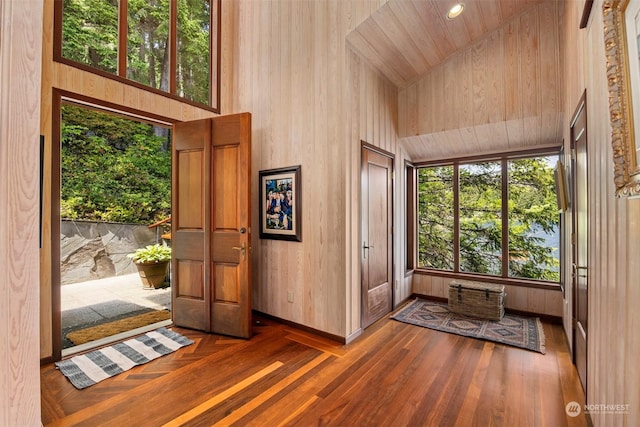 foyer entrance featuring dark hardwood / wood-style flooring, high vaulted ceiling, and wood walls