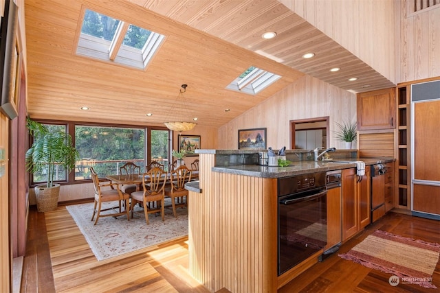 kitchen featuring pendant lighting, sink, lofted ceiling with skylight, oven, and light wood-type flooring