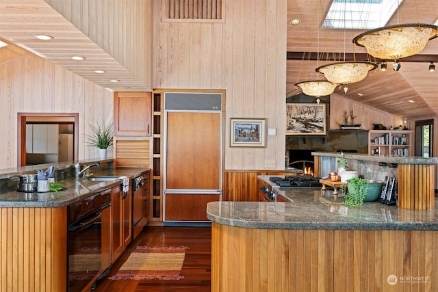 kitchen with vaulted ceiling with skylight, black oven, sink, dark hardwood / wood-style flooring, and paneled built in fridge