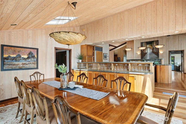 dining space with lofted ceiling, wooden walls, light wood-type flooring, and wooden ceiling