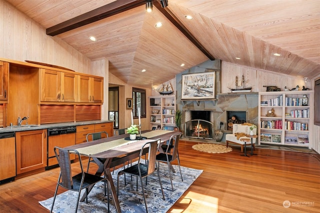 dining space with a stone fireplace, vaulted ceiling with beams, sink, and light hardwood / wood-style floors