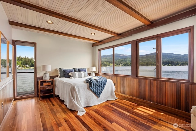 bedroom featuring access to exterior, beam ceiling, wooden walls, a water and mountain view, and wood-type flooring