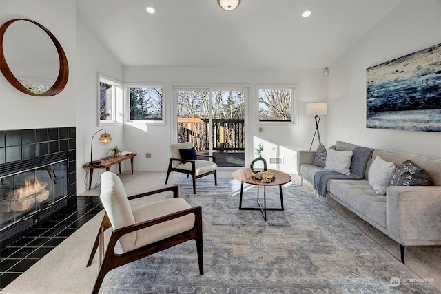 living room with a tiled fireplace, vaulted ceiling, and dark tile patterned flooring