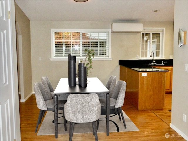 dining space with sink, light hardwood / wood-style floors, and an AC wall unit