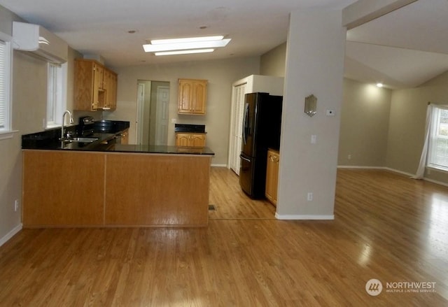 kitchen featuring lofted ceiling, sink, light hardwood / wood-style flooring, black refrigerator, and kitchen peninsula