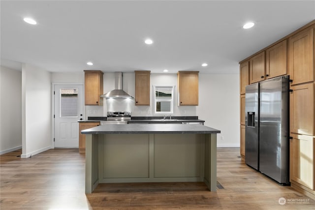 kitchen featuring wall chimney range hood, a kitchen island, light hardwood / wood-style floors, and appliances with stainless steel finishes