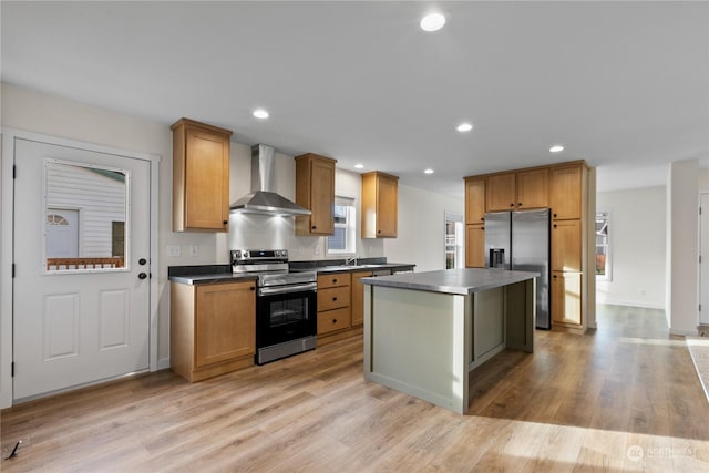 kitchen featuring wall chimney exhaust hood, appliances with stainless steel finishes, a center island, and light wood-type flooring