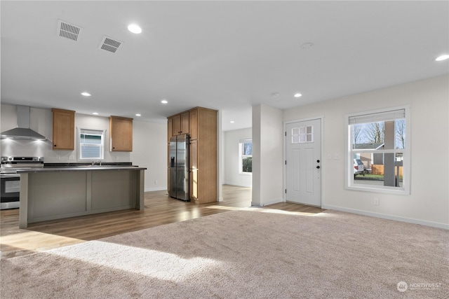 kitchen featuring wall chimney exhaust hood, stainless steel appliances, light carpet, and a wealth of natural light