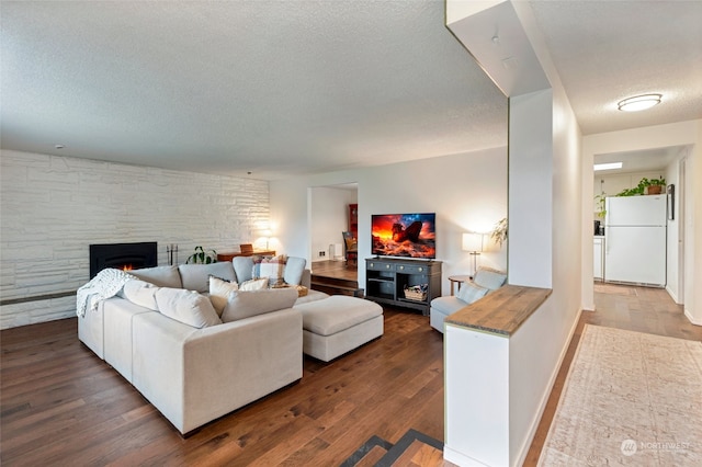 living room with dark wood-type flooring, a stone fireplace, and a textured ceiling