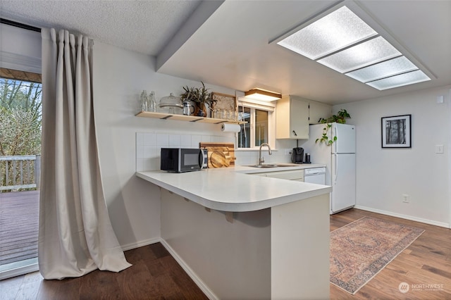 kitchen with sink, white appliances, dark wood-type flooring, backsplash, and kitchen peninsula