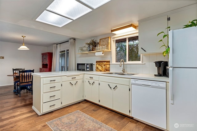 kitchen with sink, white appliances, light hardwood / wood-style flooring, hanging light fixtures, and kitchen peninsula