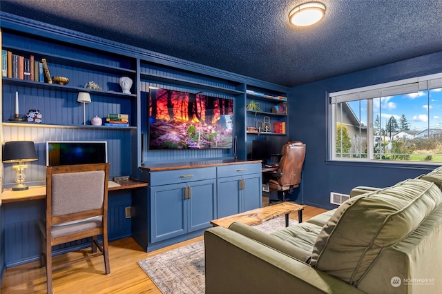 interior space featuring built in desk, a textured ceiling, and light hardwood / wood-style floors