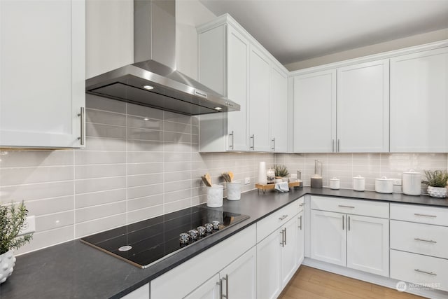 kitchen with dark countertops, decorative backsplash, white cabinetry, wall chimney range hood, and black electric cooktop