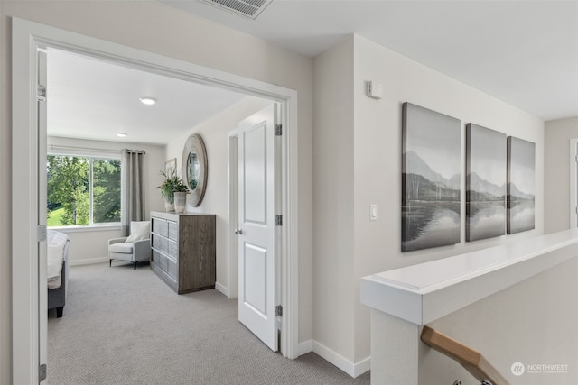 hallway featuring baseboards, visible vents, and light colored carpet