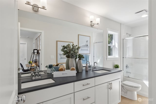 bathroom with combined bath / shower with glass door, a sink, toilet, and double vanity