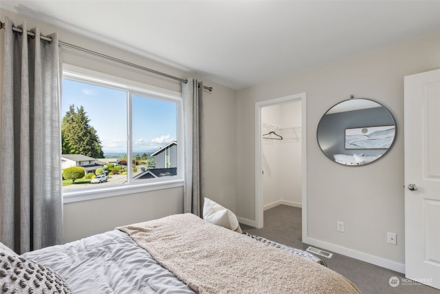 bedroom featuring a spacious closet, dark colored carpet, visible vents, and baseboards