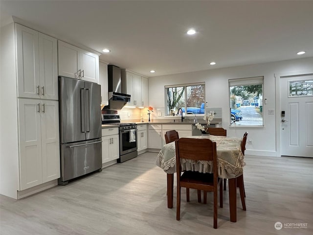 kitchen featuring wall chimney exhaust hood, stainless steel appliances, light hardwood / wood-style flooring, and white cabinets