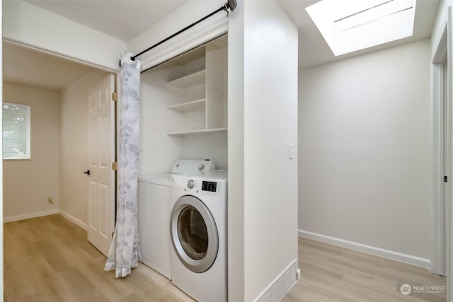 clothes washing area featuring a skylight, light hardwood / wood-style flooring, and independent washer and dryer