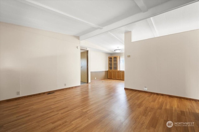 empty room featuring vaulted ceiling with beams and hardwood / wood-style flooring