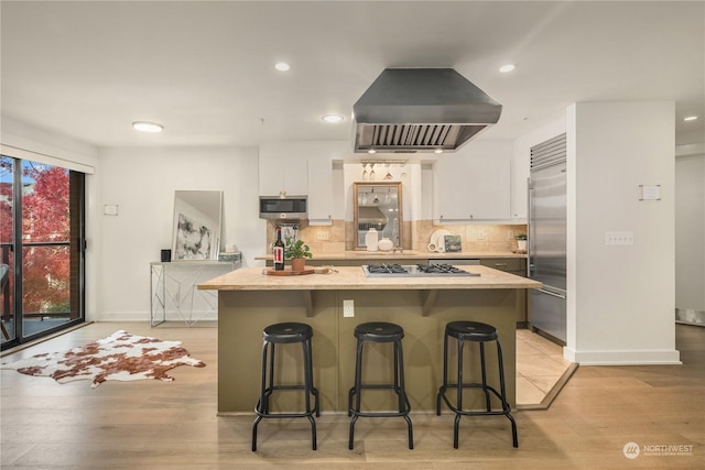 kitchen featuring a kitchen island, appliances with stainless steel finishes, a breakfast bar area, white cabinets, and exhaust hood