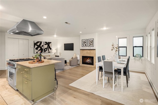 kitchen with light hardwood / wood-style flooring, a breakfast bar area, high end stainless steel range oven, a center island, and island range hood