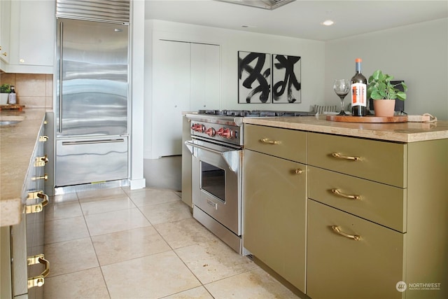 kitchen featuring premium appliances, light tile patterned floors, and green cabinets