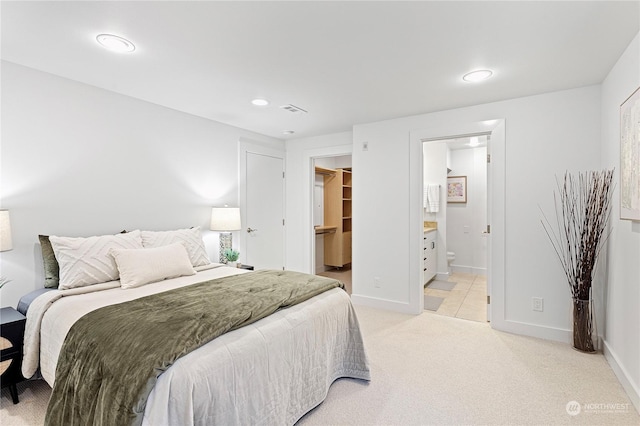 bedroom featuring light colored carpet, a spacious closet, and ensuite bath