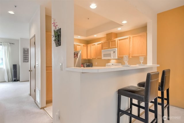 kitchen with light brown cabinetry, light carpet, a kitchen breakfast bar, and kitchen peninsula