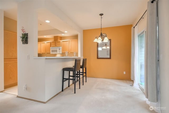 kitchen with hanging light fixtures, a kitchen bar, light colored carpet, kitchen peninsula, and light brown cabinets