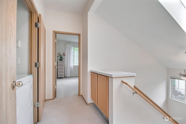 hallway featuring washer / dryer, an upstairs landing, light colored carpet, and baseboards