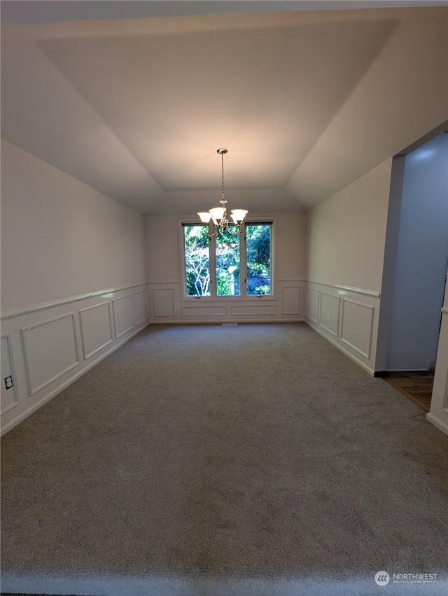 unfurnished dining area featuring an inviting chandelier, carpet floors, a raised ceiling, and vaulted ceiling