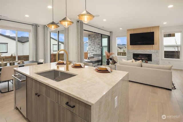 kitchen featuring decorative light fixtures, an island with sink, sink, stainless steel dishwasher, and light hardwood / wood-style flooring