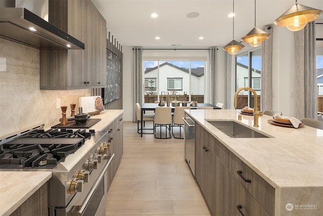 kitchen featuring pendant lighting, wall chimney range hood, sink, stainless steel appliances, and tasteful backsplash