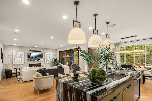 kitchen featuring hanging light fixtures, a large fireplace, sink, and light hardwood / wood-style floors