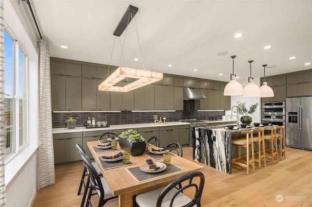 kitchen with tasteful backsplash, a center island with sink, appliances with stainless steel finishes, gray cabinets, and light hardwood / wood-style floors