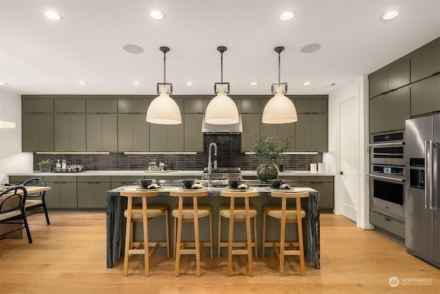 kitchen featuring a breakfast bar area, stainless steel appliances, light hardwood / wood-style floors, an island with sink, and decorative light fixtures